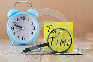 `taxes time` on a sticker with dollars and alarm clock on a wooden table. Tax concept.