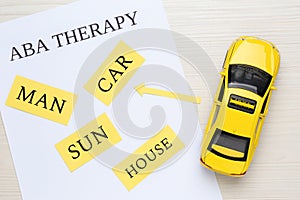 Taxi car model near sheet of paper with text ABA Therapy and different words on white wooden table, flat lay. Applied behavior