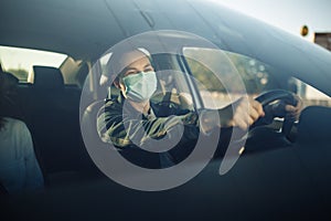 Taxi driver wearing sterile medical mask hold his hands on the steering wheel. Young man drives a car with a passenger