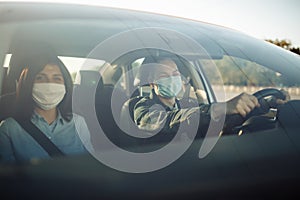 Taxi driver wearing sterile medical mask hold his hands on the steering wheel. Young man drives a car with a passenger