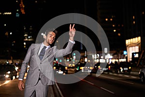 Taxi. A handsome businessman hailing a cab while standing in a busy city street at night.