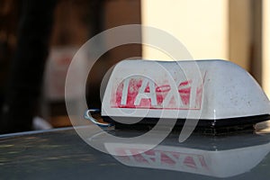 Taxi light sign or cab sign in drab white and fade away red color with white text on the car roof at the street