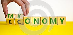 Taxonomy or economy symbol. Businessman turns cubes, changes the word economy to taxonomy. Beautiful yellow table, white