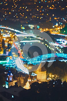 Tbilisi, Georgia. Abstract Blurred Bokeh Urban Backdrop Of Sioni Cathedral And Bridge Of Peace At Evening Night Street
