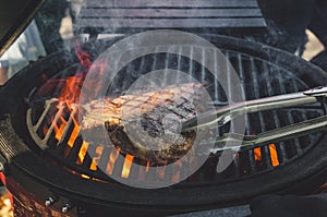 Tbone beef steak being cooked on a grill with tongs photo