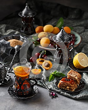 Tea armud in Turkish style with lemon. served on a silk tablecloth with baklava and fruit-cherries and apricots