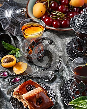 Tea armud in Turkish style with lemon. served on a silk tablecloth with baklava and fruit-cherries and apricots