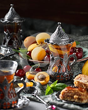 Tea armud in Turkish style with lemon. served on a silk tablecloth with baklava and fruit-cherries and apricots