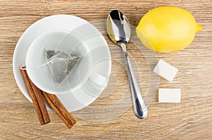 Tea bag in cup, cinnamon sicks on saucer, lemon, sugar photo