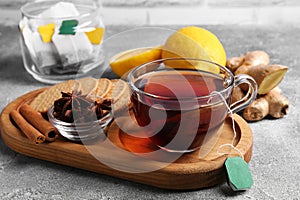 Tea bags, cup of hot drink, cookies and ingredients on light grey table