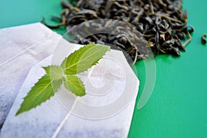 Tea bags, loose tea and fresh mint leaves on a green background