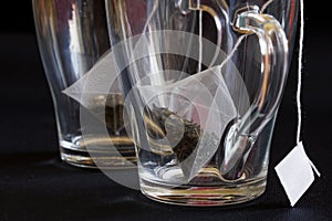 Tea bags - pyramids with ropes and tags in transparent heat-resistant glass mugs. Macro. Green tea