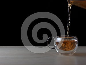 Tea being poured into double sided glass cup from glass saucer