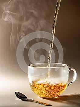 Tea being poured into glass tea cup with steam on brown monochrome background