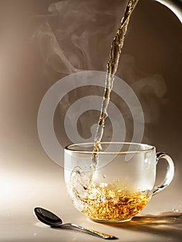 Tea being poured into glass tea cup with steam on brown monochrome background