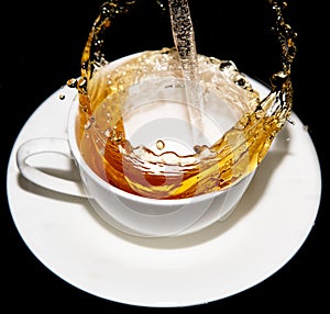 Tea being poured into a saucer with splashes on a black background