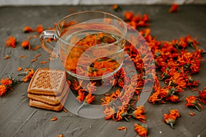 Tea with calendula flowers and biscuits. Transparent glass cup and saucer