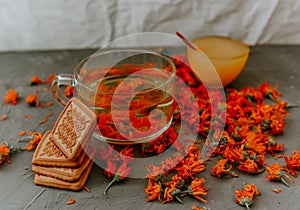 Tea with calendula flowers and biscuits. Transparent glass cup and saucer