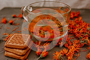 Tea with calendula flowers and biscuits. Transparent glass cup and saucer