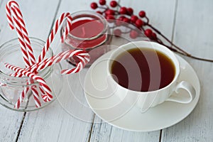Tea, candle, Christmas canes and berries on a white wooden background