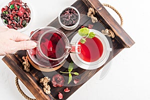 Tea ceremonia . a woman`s hand pours fragrant red hibiscus tea into a cup of mint leaves. top view of the wooden tray with mornin photo