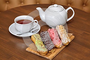 Tea and colorful eclair cakes with cream on wooden board