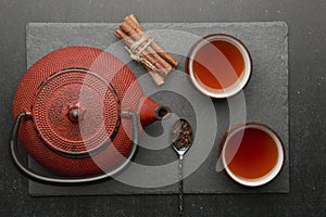 Tea composition with ceramic tea cups and red iron teapot on dark stone background