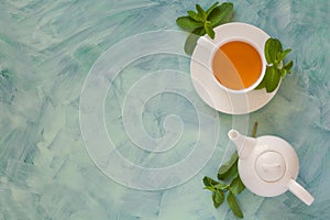 Tea concept. Teapot and cup with green herbal tea decorated mint leaves on wooden background.