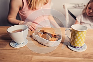 Tea and cookies for breakfast on wooden table with mother and baby on background