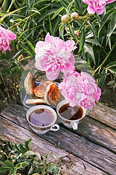 Tea in country style in summer garden in the village. Two cups of black tea and pancakes on wooden boards and blooming peony