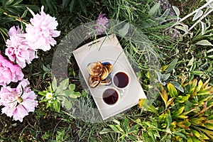 Tea in country style in summer garden in the village. Two cups of black tea and pancakes on wooden tray and blooming peony flowers