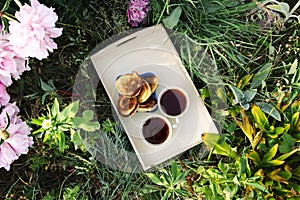 Tea in country style in summer garden in the village. Two cups of black tea and pancakes on wooden tray and blooming peony flowers