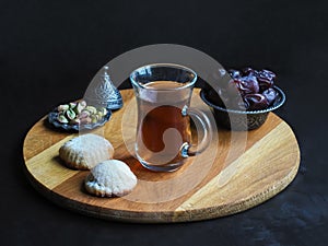 Tea cup with Egyptian cookies `Kahk El Eid` and dates on the black table.