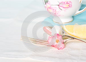 Tea Cup, Fork and Spoon with sugar cube and lemon on white table cloth