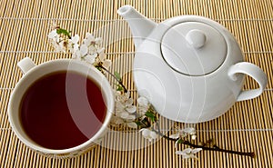 Tea in a cup and teapot, fresh flowers on a background of bamboo boards