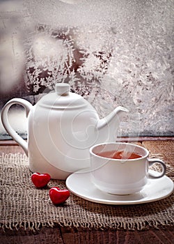 Tea cup and teapot with red hearts in winter frosty day