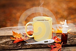 Tea cup with thermometer, autumn leaves and nose drops, flu seas