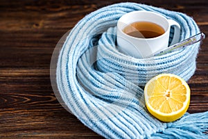 Tea cup with thermometer, blue scarf and lemon on wooden background. Flu season, disease