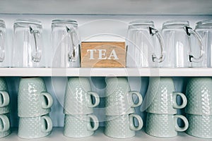 Tea cups and coffee mugs on a kitchen shelf with a tea box Rack focus. Close up.