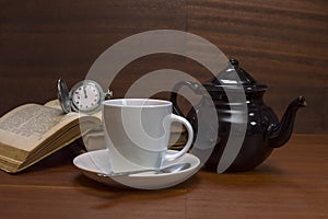 Tea cups with teapot, books and old pocket watch on wooden table