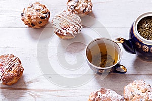 Tea cups, teapot and muffins on white wooden table, set teapot and brewed tea with cakes on table, green black herbal hot beverage