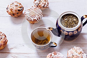 Tea cups, teapot and muffins on white wooden table, set teapot and brewed tea with cakes on table, green black herbal hot beverage