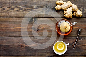 Tea for cure colds. Cup, teapot, ginger root and lemon on dark wooden background top view copy space