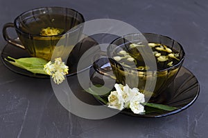 Tea and flowers. two dark glass cups with herbal hot linden tea and jasmine tea