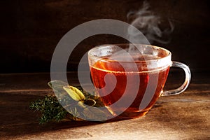 tea freshly brewed in a glass cup and some herbs on a dark rustic wooden background, healthy hot drink against cold and flu, copy