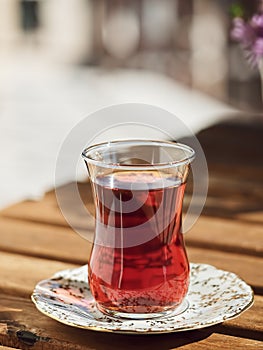 Tea in a glass of armudu on a saucer, located on a wooden table in the loggia. In the background are flowers . Bright sunny day.