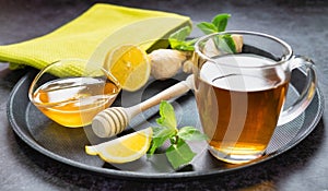 Tea in a glass cup with honey,ginger and lemon on a tray with green cloth image