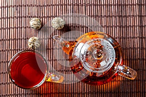 Tea in a glass teapot with a blooming large flower. Teapot with exotic green tea-balls blooms flower and a glass Cup of tea. Tea