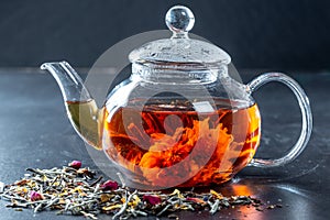 Tea in a glass teapot with a blooming large flower. Teapot with exotic green tea-balls blooms flower and dried tea and rose buds