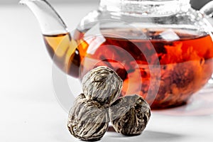 Tea in a glass teapot with a blooming large flower. Teapot with exotic green tea on a white background with dried balls-buds for